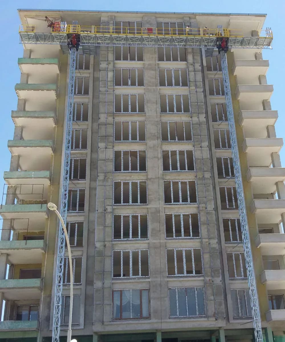 Çift kule cephe asansörü, çok katlı bir binanın cephesinde iki dikey kule üzerinde konumlanmış geniş çalışma platformuyla